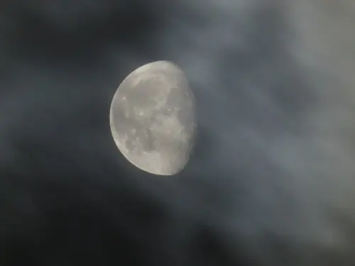A three-quarter's full moon floating through clouds.