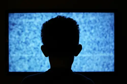 The silhouette of a man sitting in front of a television displaying static.