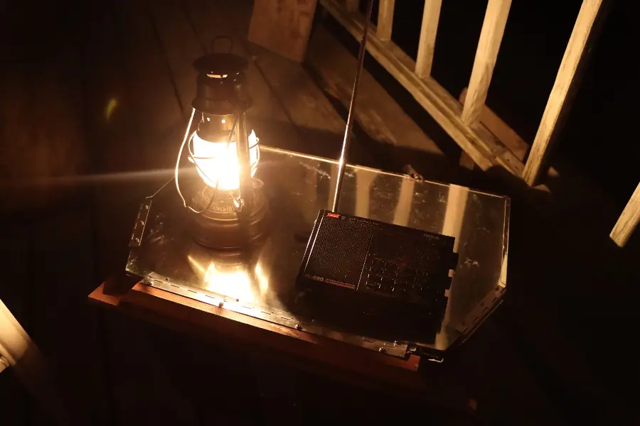 A lit hurricane lantern and portable shortwave radio, sitting on a low table on a deck at nighttime.