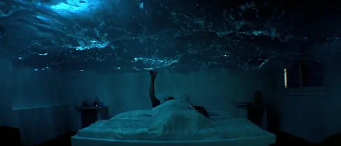 Jack laying in bed, appearing to be submerged underwater. He reaches up to the surface of the water.